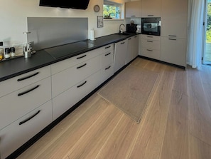 Une cuisine moderne avec un plan de travail noir, des appareils en acier inoxydable et un revêtement de sol en bois clair.