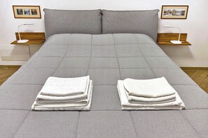 A neatly made bed with grey bedding, two pillows, and two bedside tables with lamps. - Traditional Roman hospitality, right next to St. Peter’s! (Roma)