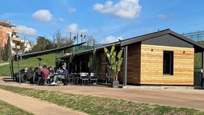 Un petit bâtiment en bois avec un toit en pente, des places assises à l’extérieur et un chemin piétonnier dallé.