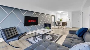 A modern living room with a flat-screen TV, a sofa, a chair, and a dining area. - 17th Ave Nest in Downtown , Walk to Stampede Grounds (Calgary)