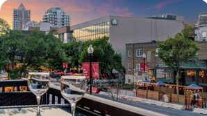 A cityscape with modern buildings, a waterfront promenade, and outdoor dining areas. - 17th Ave Nest in Downtown , Walk to Stampede Grounds (Calgary)