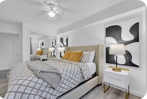 Ein Schlafzimmer mit Bett, Nachttisch, Lampe und abstrakter Wandkunst.