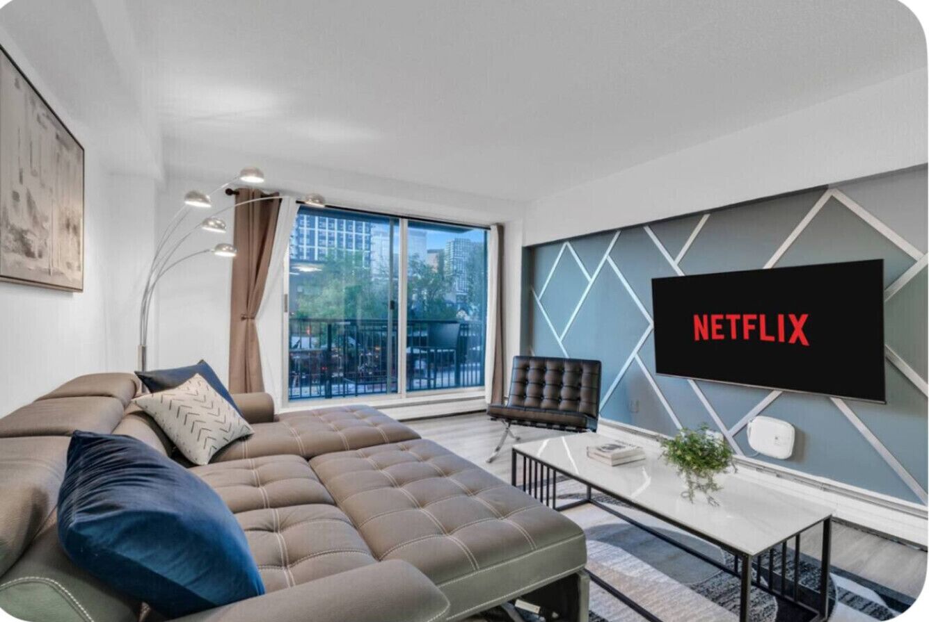 Una sala de estar moderna con un televisor de pantalla plana grande, un sofá, una mesa de centro y vistas de la ciudad a través de amplias ventanas.