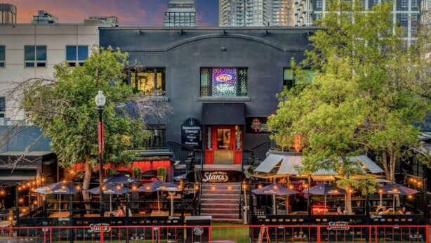 A building with a bar and outdoor seating, surrounded by trees and urban buildings. - 17th Ave Nest in Downtown , Walk to Stampede Grounds (Calgary)
