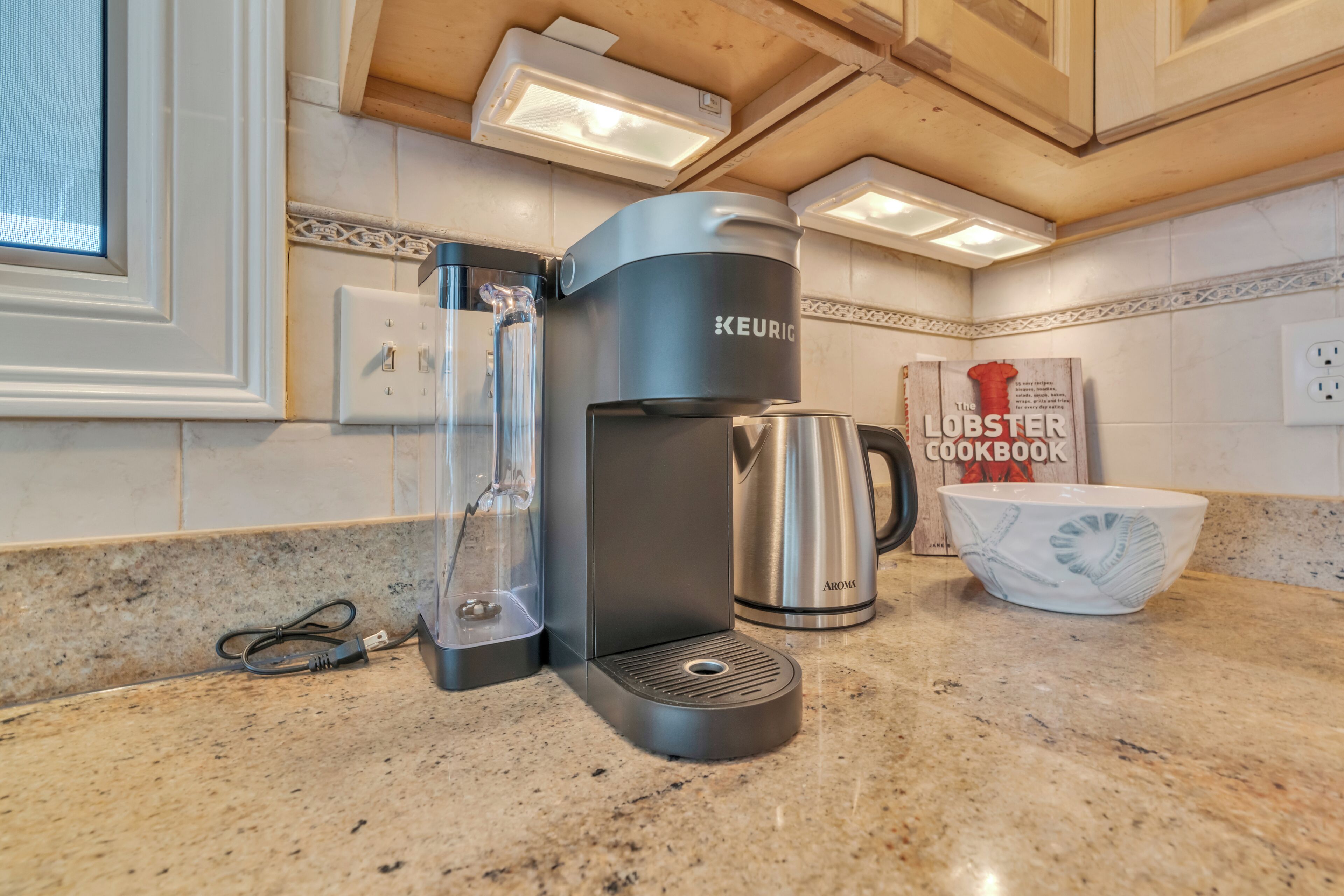 Una cucina con una macchina per caffè Keurig, una caraffa di vetro, una caffettiera in acciaio inossidabile e un libro di cucina sui aragostini.