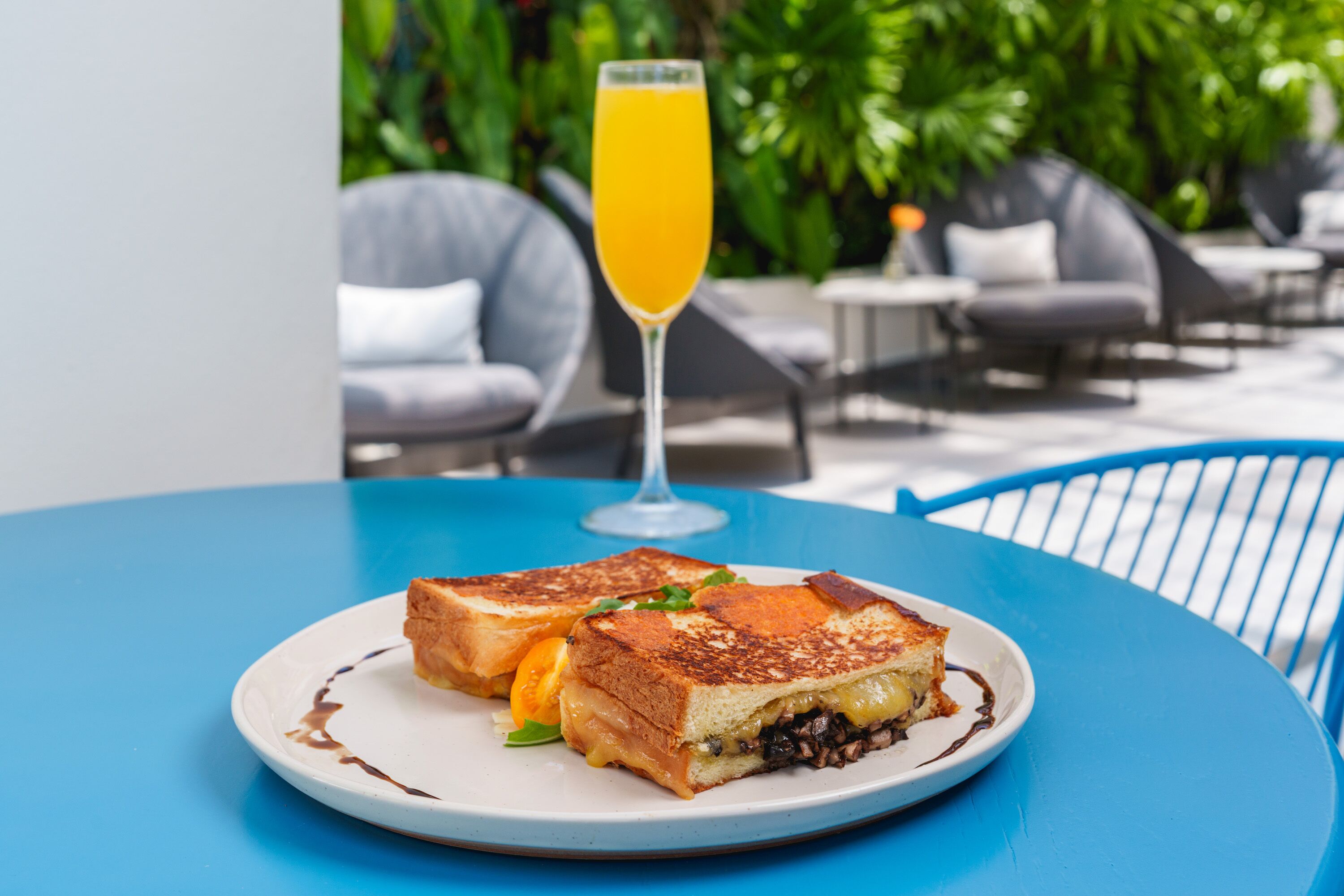 Un plato con un sándwich a la plancha y un vaso de jugo de naranja sobre una mesa azul.