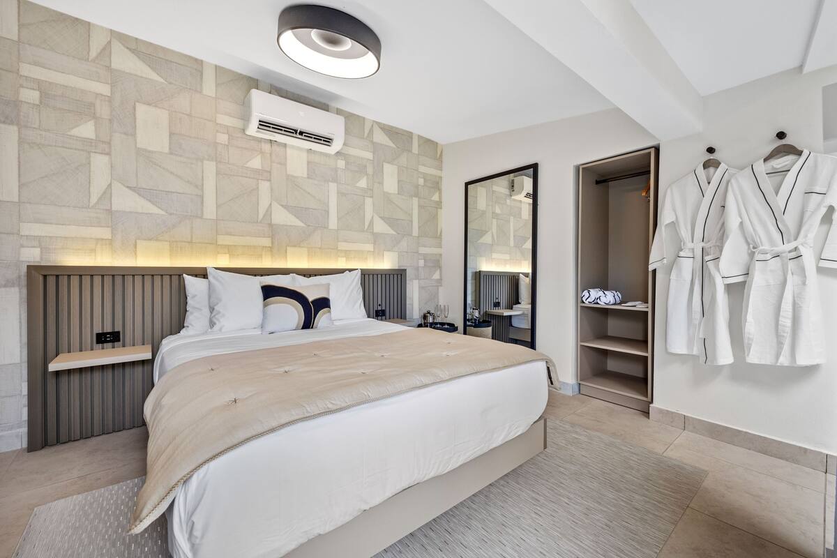 Un dormitorio moderno de hotel con una cama grande, mesitas de noche, un armario y un espejo.