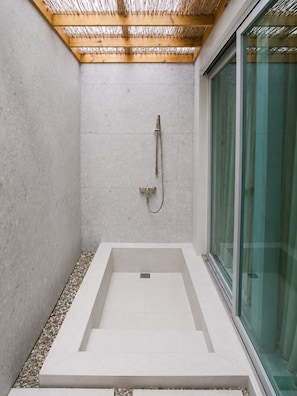 A modern shower with a wooden ceiling, a glass door, and a concrete floor.