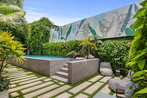 Un patio moderno al aire libre con piscina, escalones de piedra y exuberante vegetación.