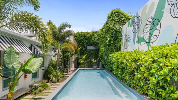 A swimming pool with tiled edges, surrounded by lush greenery and a wall with a floral mural.