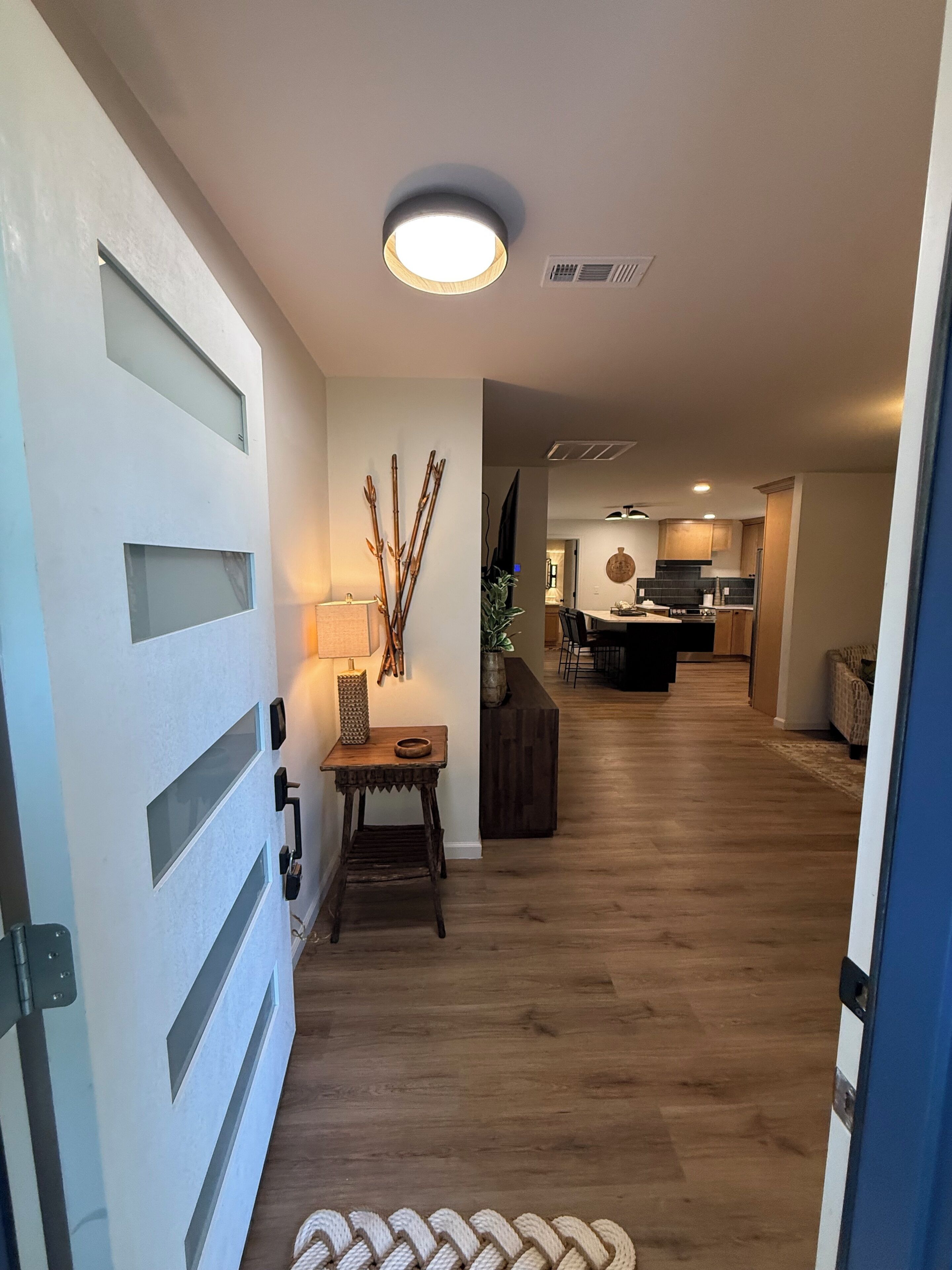 Un couloir doté d’un plancher en bois, d’une table avec une lampe et d’un luminaire fixé au mur.