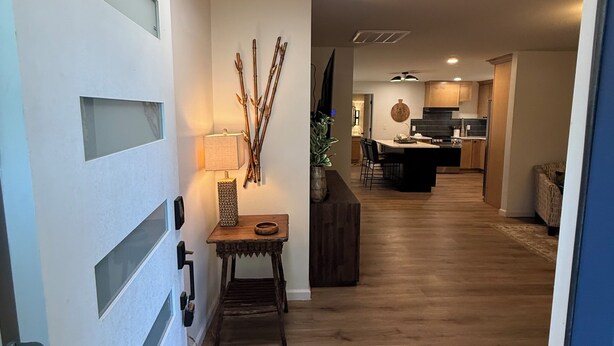 Un pasillo con suelo de madera, una mesa con lámpara y una lámpara fijada a la pared.