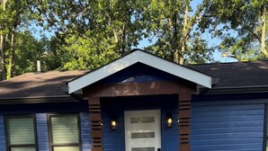 Una casa con fachada azul, puerta principal blanca y porche delantero de concreto.