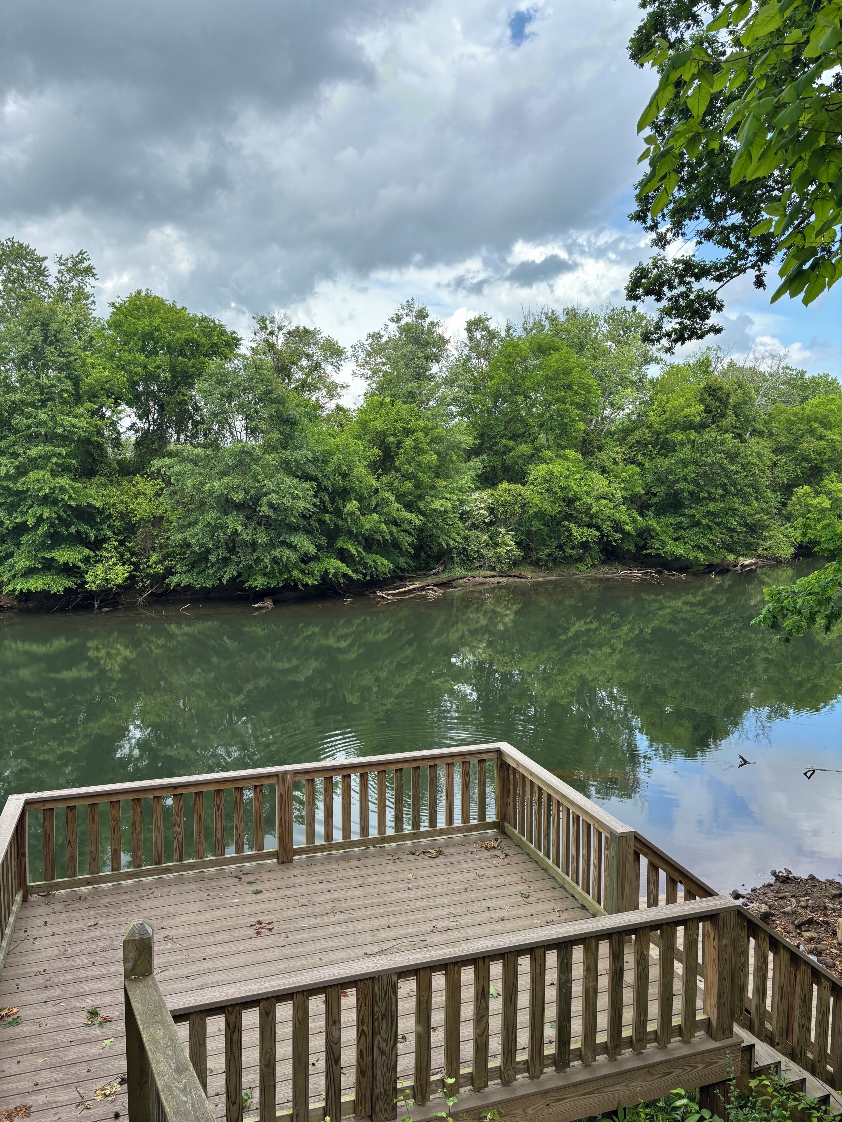 A wooden deck overlooking a calm river with dense greenery on both sides.