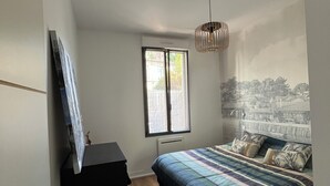 Un dormitorio con cama, cómoda, ventana con persianas, lámpara colgante y un mural en la pared.