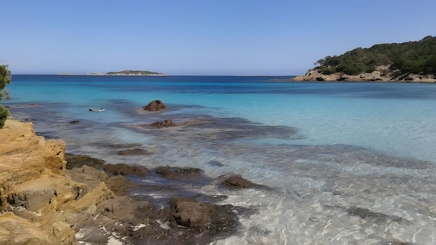 A coastal landscape with clear waters, rocky shorelines, and distant landforms.
