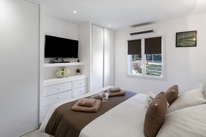A bedroom with a bed, a television, a window with blinds, and an air conditioning unit. - Villa la Chiappa: Seaside, Heated Pool & Jacuzzi (Porto-Vecchio)