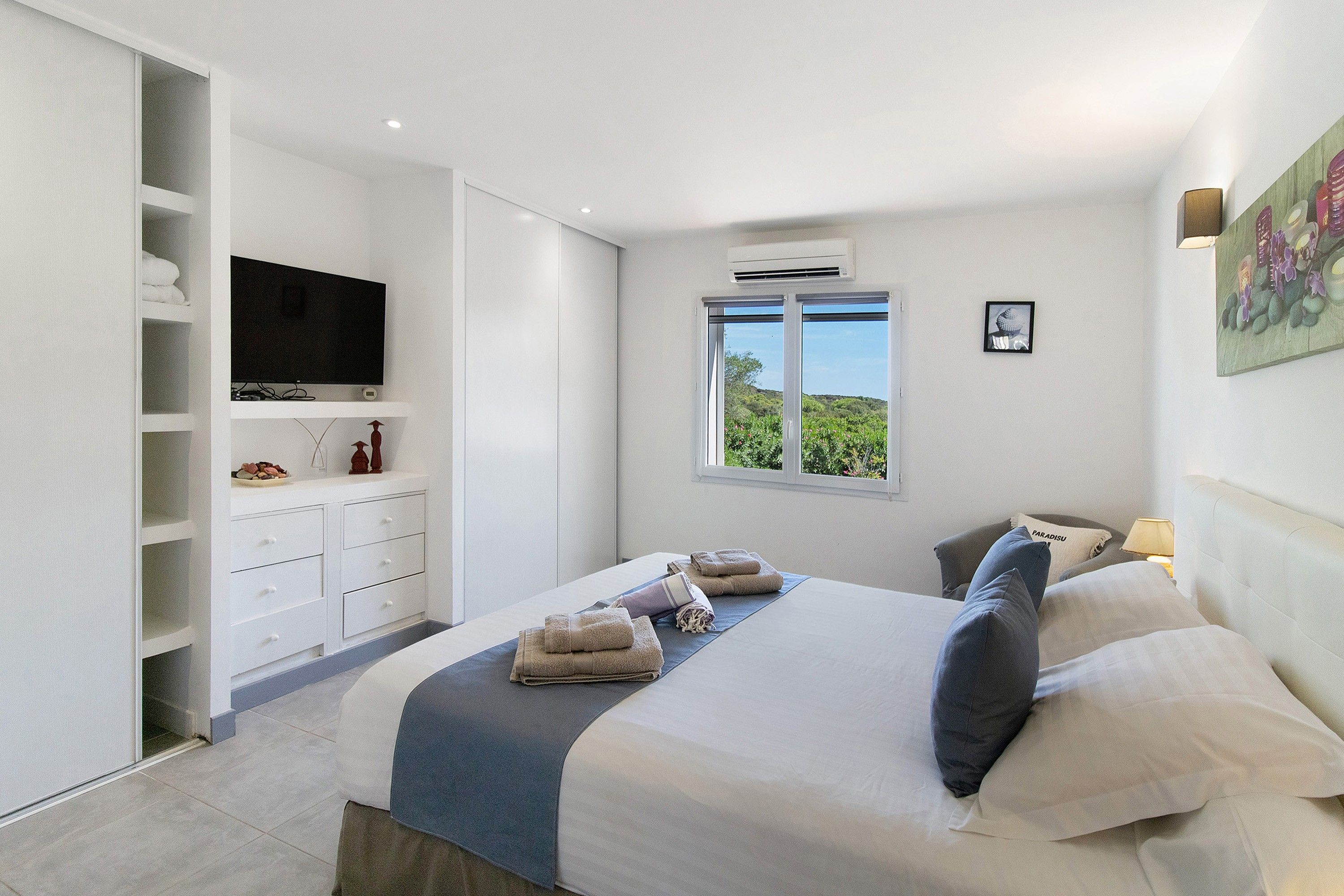 A bedroom with a bed, a television, a window with a view, and a wardrobe.