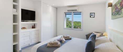 A bedroom with a bed, a television, a window with a view, and a wardrobe.