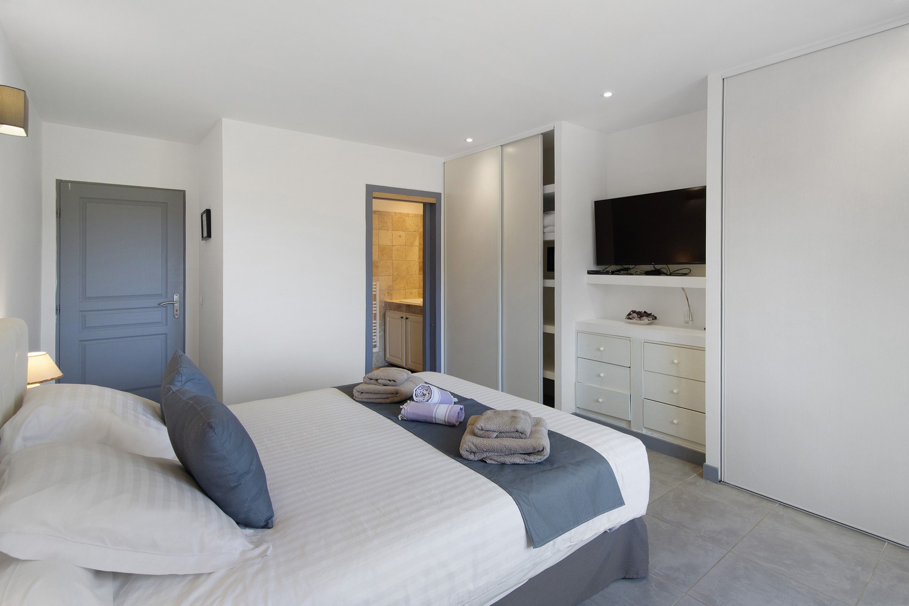 A modern bedroom with a bed, a TV mounted on the wall, and a wardrobe.