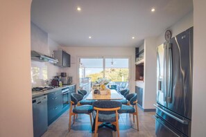 Een moderne keuken met een eetgedeelte, roestvrijstalen apparatuur en een groot raam.