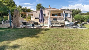 Una casa de dos pisos con piscina, mobiliario exterior y un pilar de piedra.