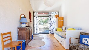 A room with a wooden floor, a sofa with a yellow pillow, a chair with a number 5 pillow, a wooden cabinet, and a lamp. - Villa “Golf” with Shared Pool, Private Terrace, and Private Garden (Moliets-et-Maa)