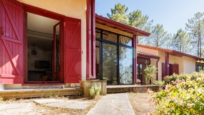 A building with red shutters, a large glass window, and a stone pathway leading to the entrance. - Villa “Golf” with Shared Pool, Private Terrace, and Private Garden (Moliets-et-Maa)