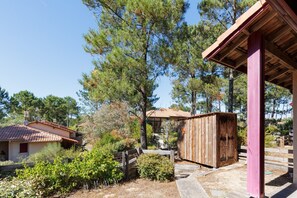 Une cabane rustique avec un toit en tuiles, entourée de pins et d’une clôture en bois.
