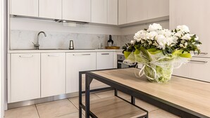 A modern kitchen with white cabinets, a marble backsplash, a stainless steel faucet, a coffee machine, and a vase with white flowers.