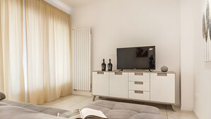 A modern living room with a sofa, a flat-screen TV, a white cabinet, and a radiator.