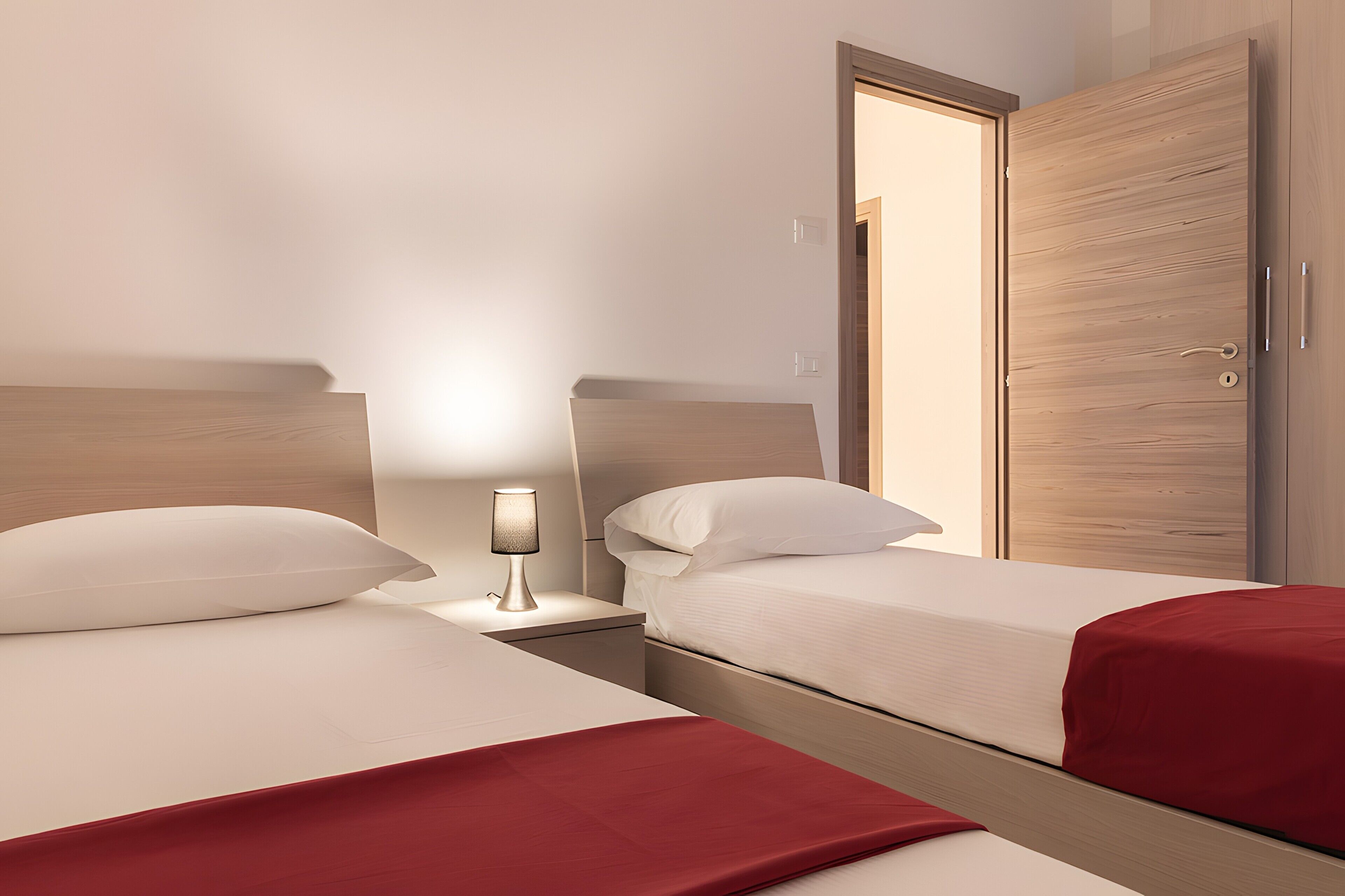 Une chambre d’hôtel avec deux lits, une table de chevet avec une lampe et une armoire en bois.