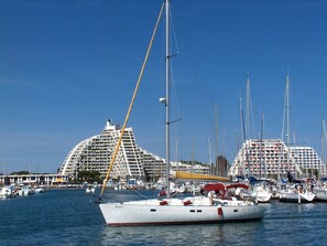 A marina with multiple sailboats docked, a prominent building with a unique architectural design, and a clear blue sky. - Les Grenadines by Interhome (La Grande Motte)