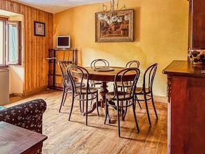 A dining area with a wooden table and chairs, a painting on the wall, and a television on a stand.