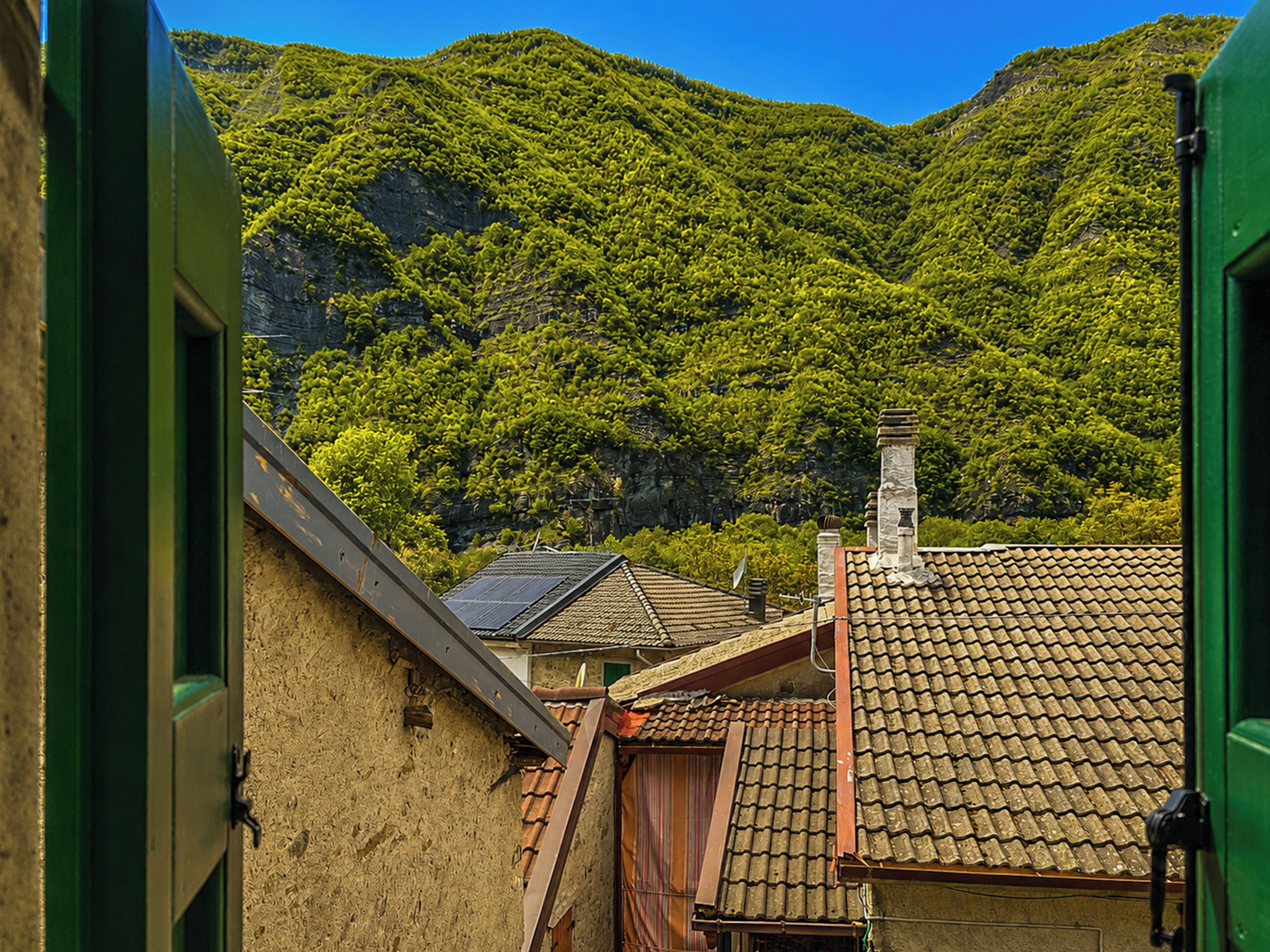 Blick auf einen Berg mit üppigem Grün und ein Gebäude mit einem Ziegeldach und Schornstein.