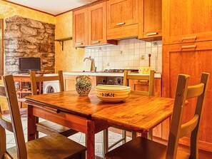 A kitchen with wooden cabinets, a stone wall, a sink, and a dining table with chairs.