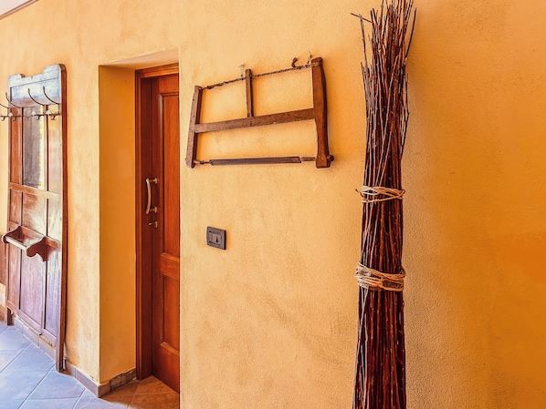 A hallway with a wooden door, a wall-mounted light switch, and a wall-mounted rack with sticks.