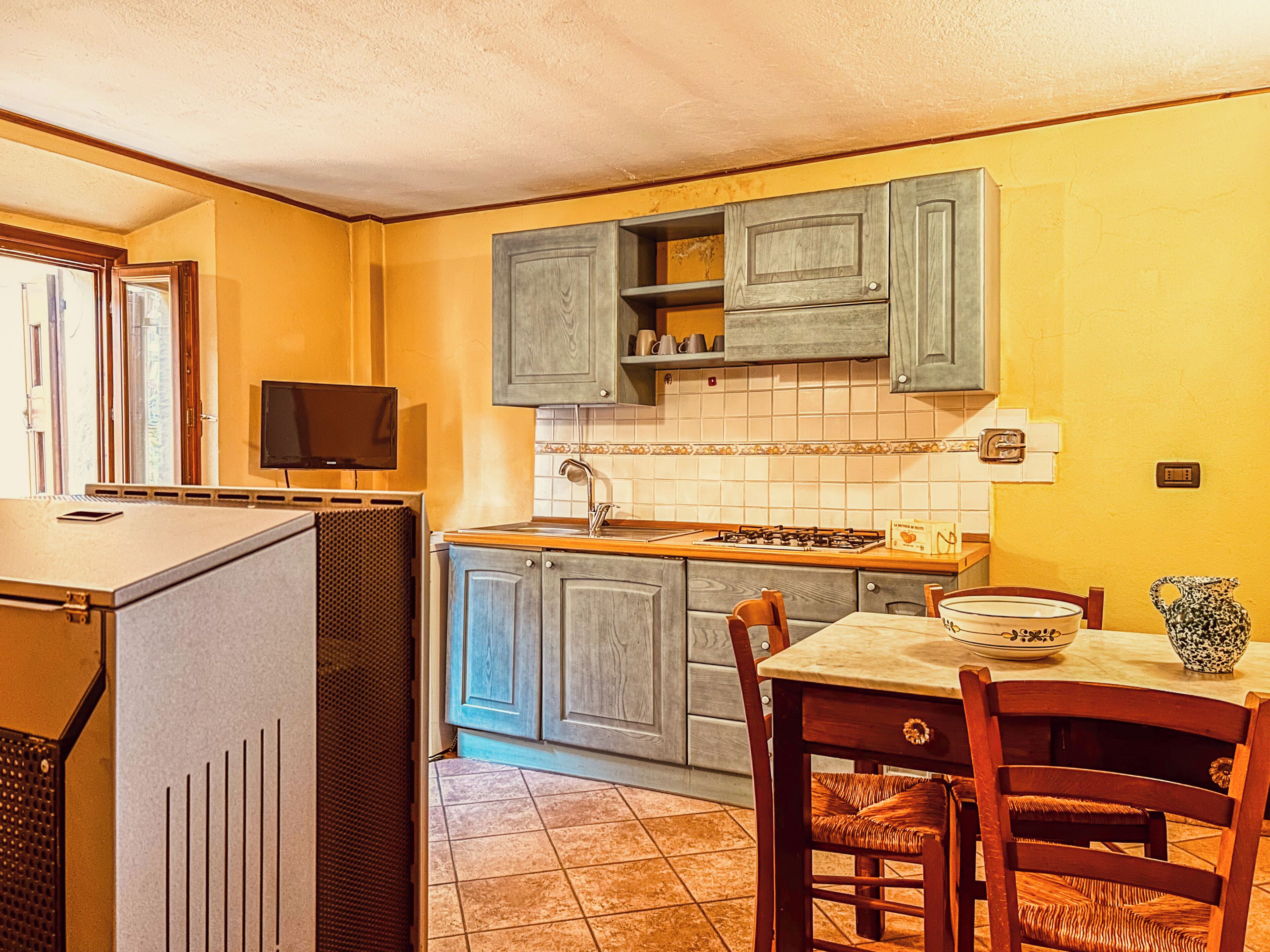 Una cucina compatta con mobili in legno, zoccolo in piastrelle, piano cottura a gas e tavolo con sedie.