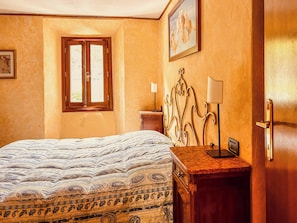 Une chambre à coucher avec un lit, une table de chevet, une lampe, une porte et une fenêtre.
