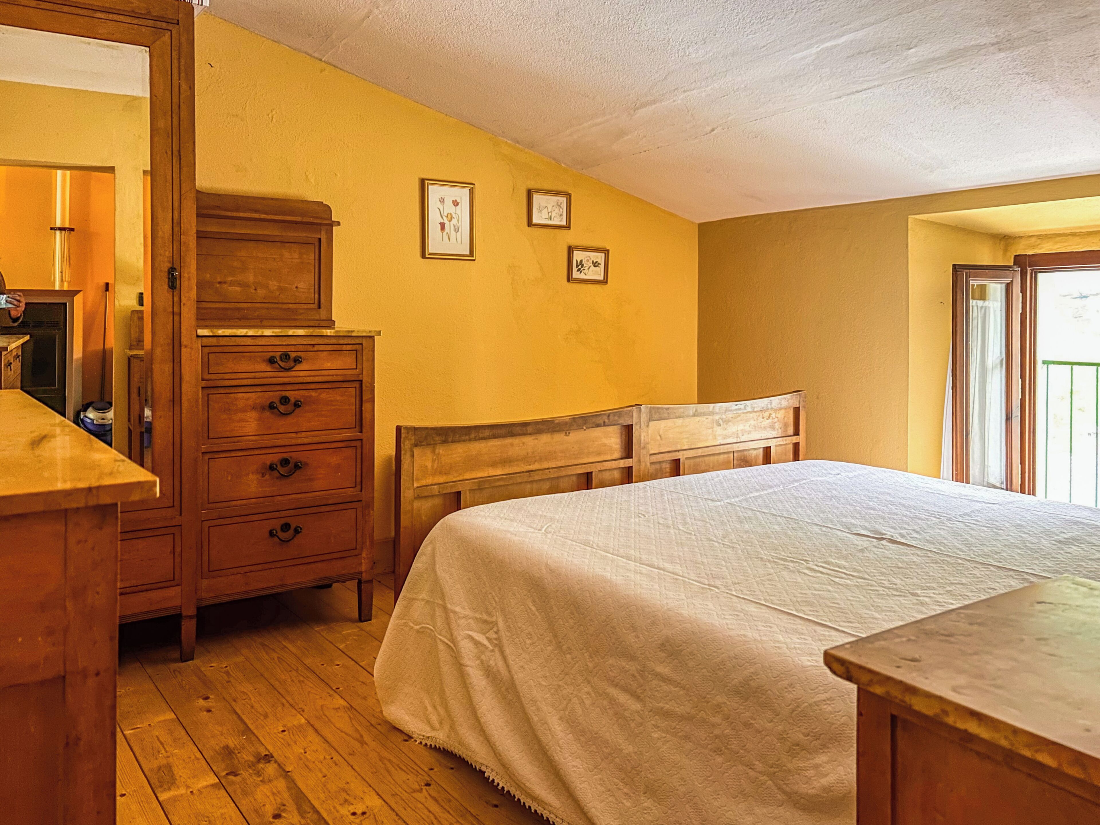 Ein Schlafzimmer mit einem hölzernen Schminktisch, einem Bett mit weißer Bettdecke und einer Tür zu einem anderen Raum.