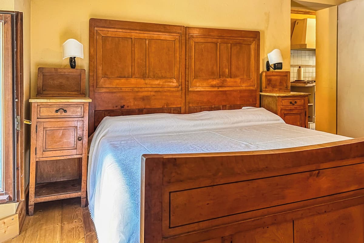 A bedroom with a wooden bed, a nightstand, a dresser, and a mirror.
