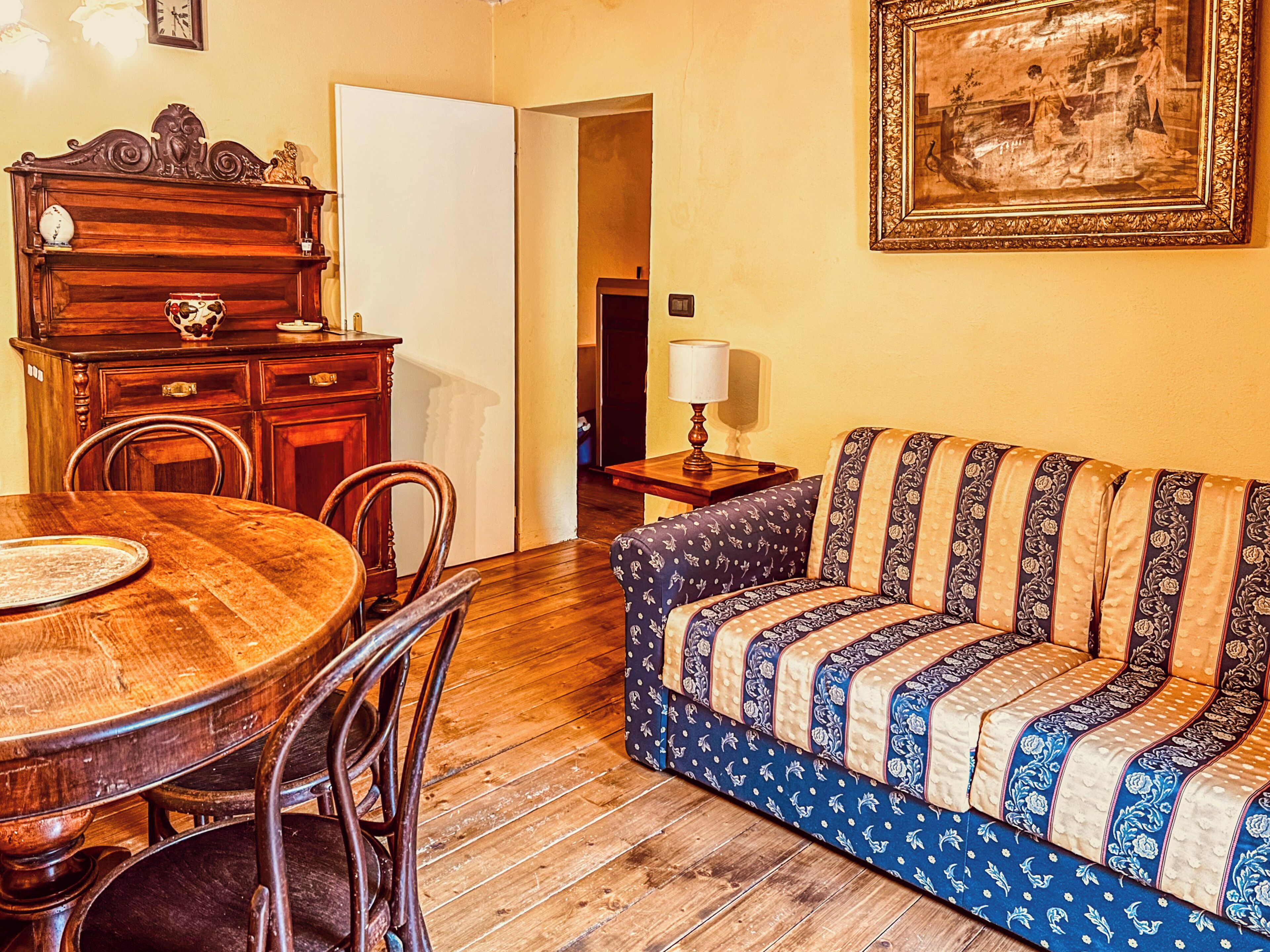 Un coin repas avec une table et des chaises en bois, un canapé recouvert d’un tissu à motifs et un tableau encadré au mur.