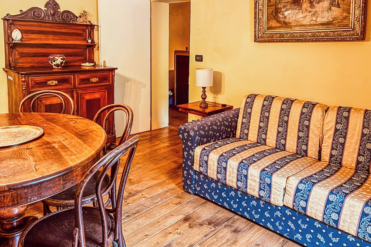 Ein Essbereich mit Holztisch und Stühlen, einer Couch mit gemustertem Bezug und einem gerahmten Bild an der Wand.