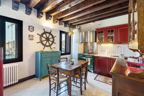 A kitchen with wooden beams, a stove, cabinets, and a dining table with chairs. - Traditional House with Fishing Boat Views in Chioggia (Chioggia)