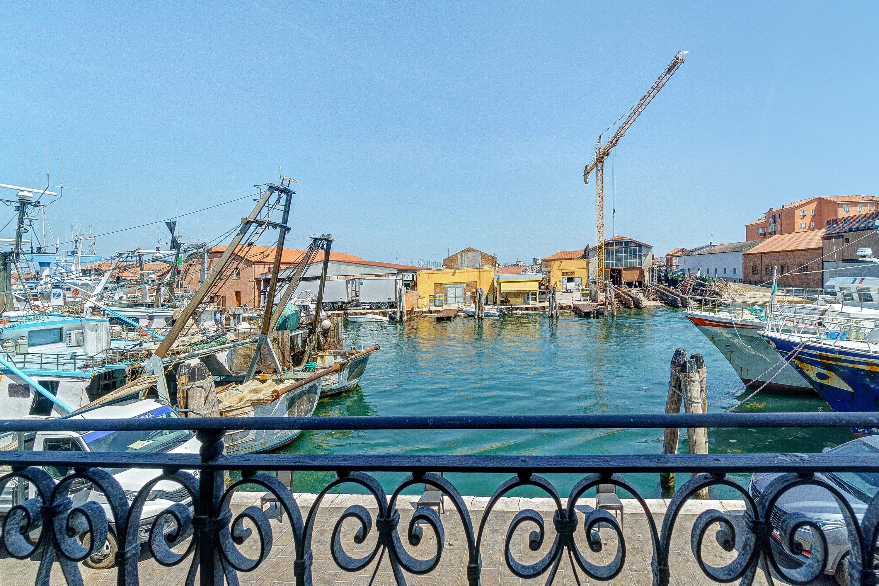 A marina with boats docked, a crane, and buildings in the background.