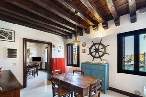 A dining area with a wooden table and chairs, a blue cabinet, and a view through a window. - Traditional House with Fishing Boat Views in Chioggia (Chioggia)