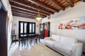 Un coin repas avec une table et des chaises en bois, un canapé blanc et un tableau floral aux couleurs vives accroché au mur.