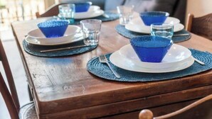 A dining table set with blue glassware and plates, placed on a wooden table with a woven placemat. - Hostdomus - Cherry Home (Alassio)