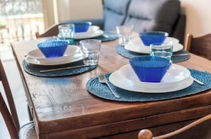 Un tavolo da pranzo apparecchiato con bicchieri e piatti azzurri, su un tavolo di legno con un sottopiattino intrecciato.