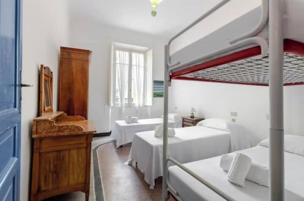 A hotel room with bunk beds, a wooden dresser, a small table, and a window with curtains.